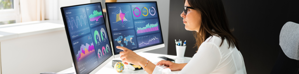 woman looking at two computer monitors with metrics and trends