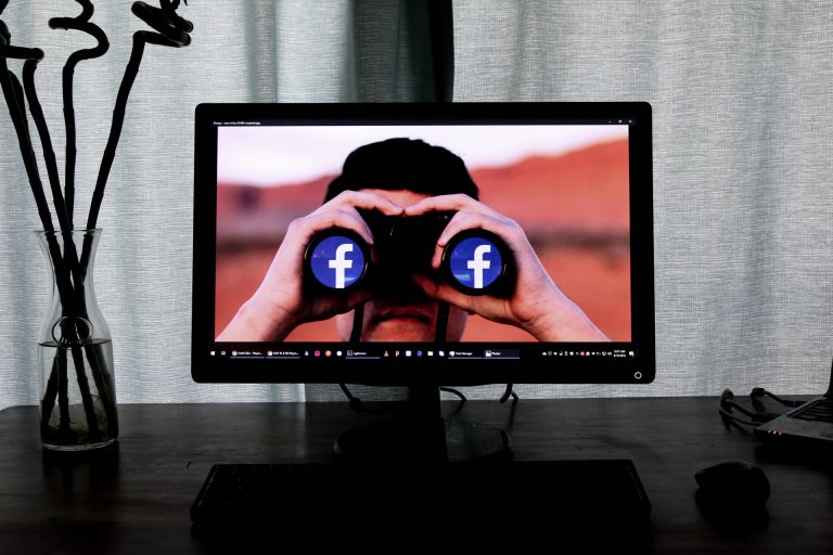 man holding binoculars on desktop with facebook logo in lenses