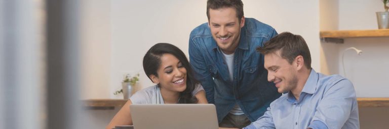 a group of 3 people looking at a computer together at the table