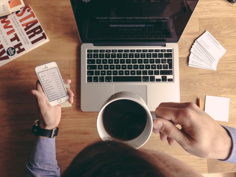 A desk with office supplies and computer and someone holding black coffee