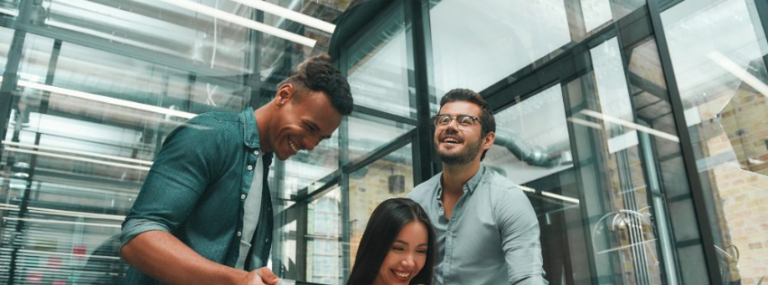 Three coworkers smiling and talking in a modern glass office.