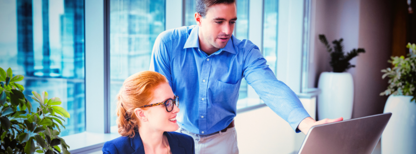 Two coworkers reviewing a laptop together in a bright office, suggesting CRM setup or team collaboration.