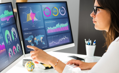 A woman looking at two monitors with different types of graphs and percentages
