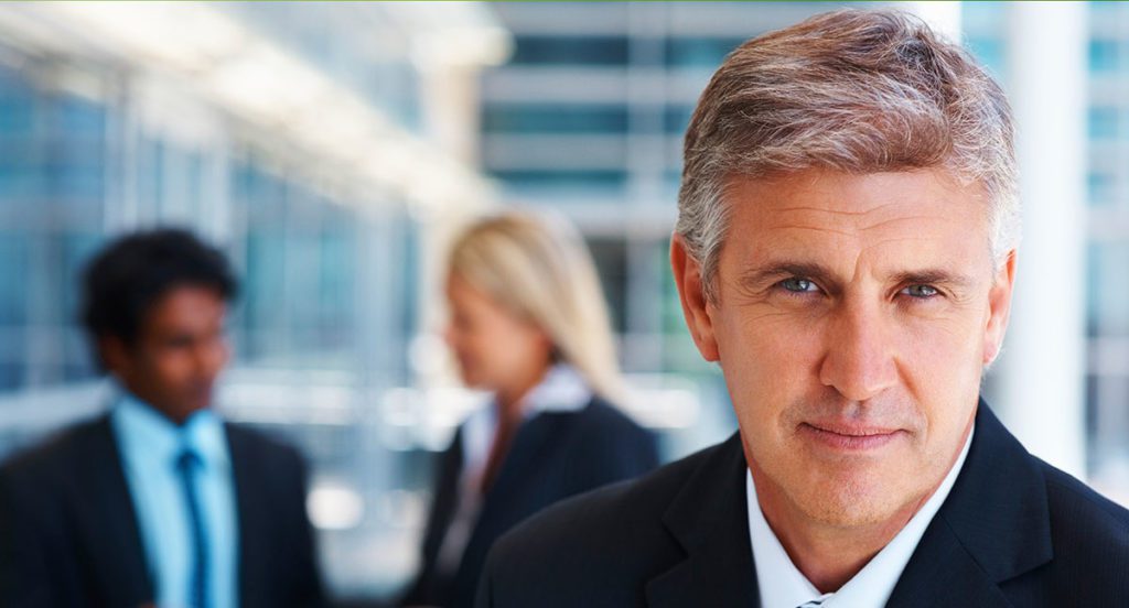 A headshot of a business man, and two people out of focus are behind him