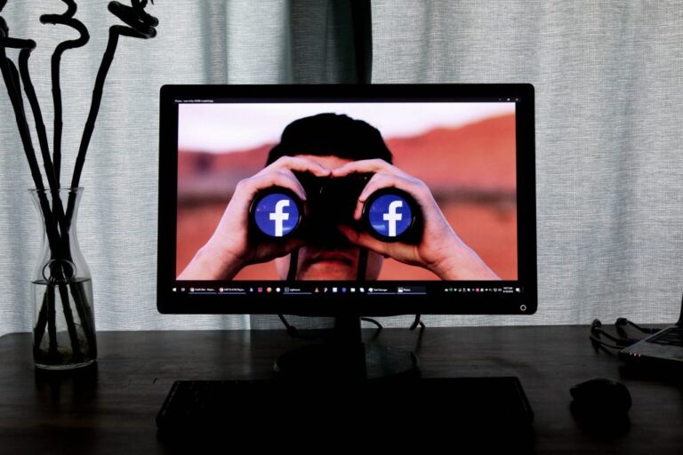 man looking through binoculars seeing facebook logo