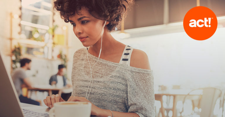 woman with headphones in working on a laptop with the act! CRM logo in the top right corner